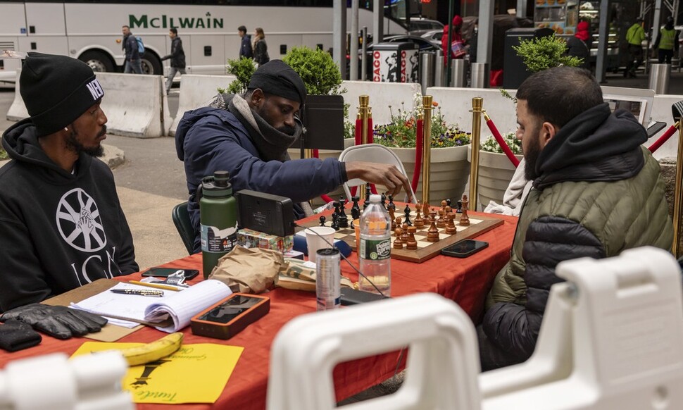 当地时间19日，尼日利亚棋手通德·奥纳科亚（中）在美国纽约时代广场与肖恩·马丁内斯（右）下棋。美联社 韩联社 新闻